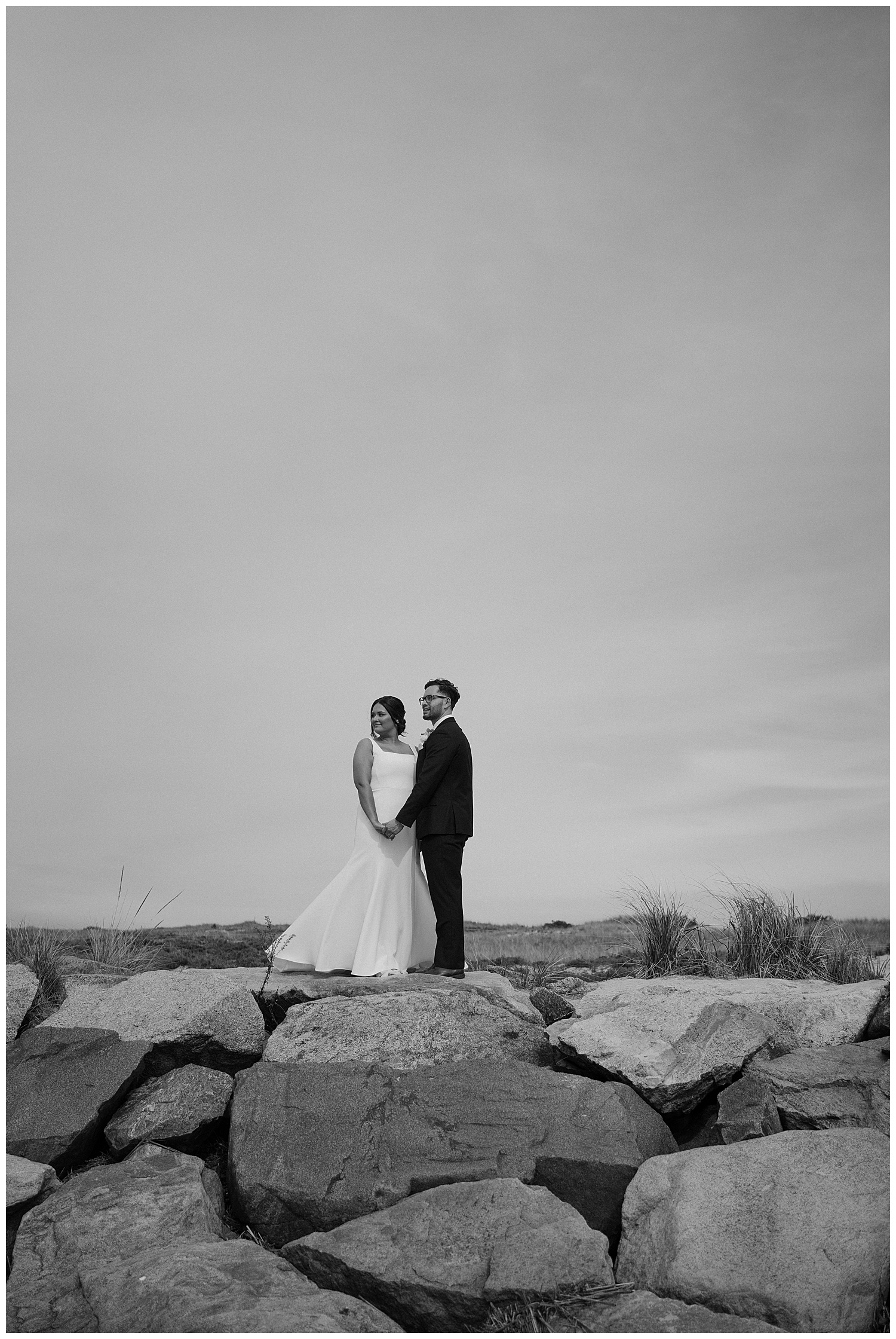 Black and White Photo of Bride and Groom standing on beach jetty